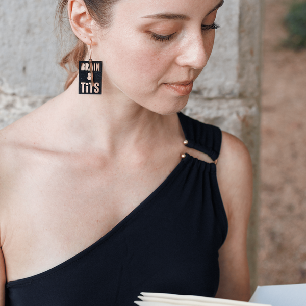 Femme portant une boucle d’oreille noire en liège gravée “Brain and Tits”, création éthique et fabriquée à la main en France par Matcha Paris.