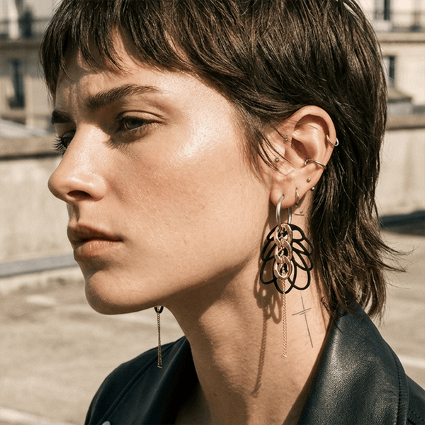 Femme portant boucles d oreilles rock asymetriques avec creoles argent, breloques noires graphiques et chaine fine, bijou createur style rock moderne et affirmé