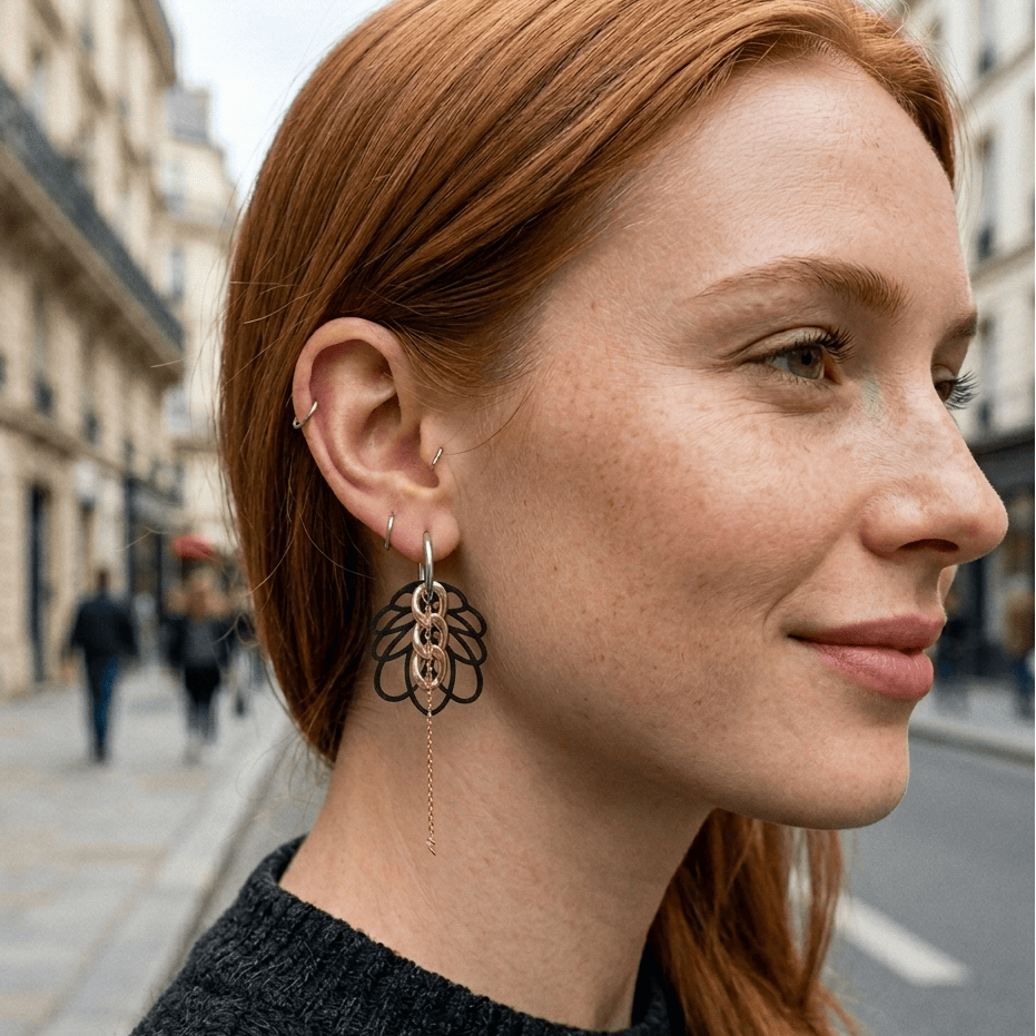 Femme rousse portant boucles d oreilles asymetriques style rock avec creoles argent, breloques noires graphiques et chaine fine, bijou createur look urbain moderne