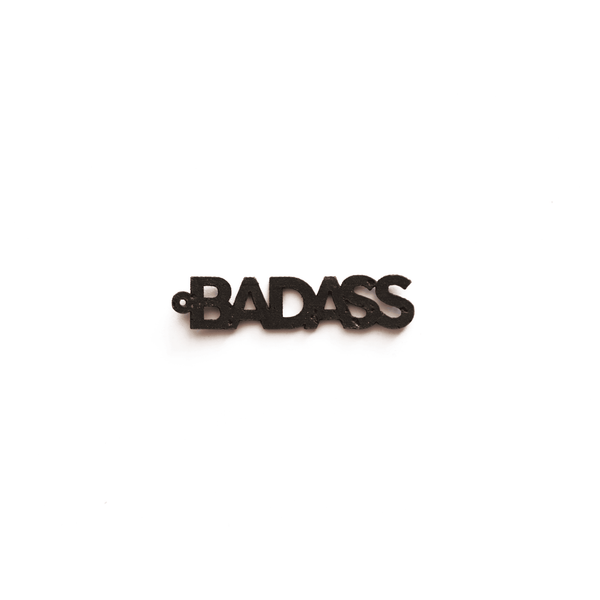 Breloque noire en forme de mot "BADASS", vue de face sur fond blanc, bijou interchangeable et éthique de la marque Matcha Paris.