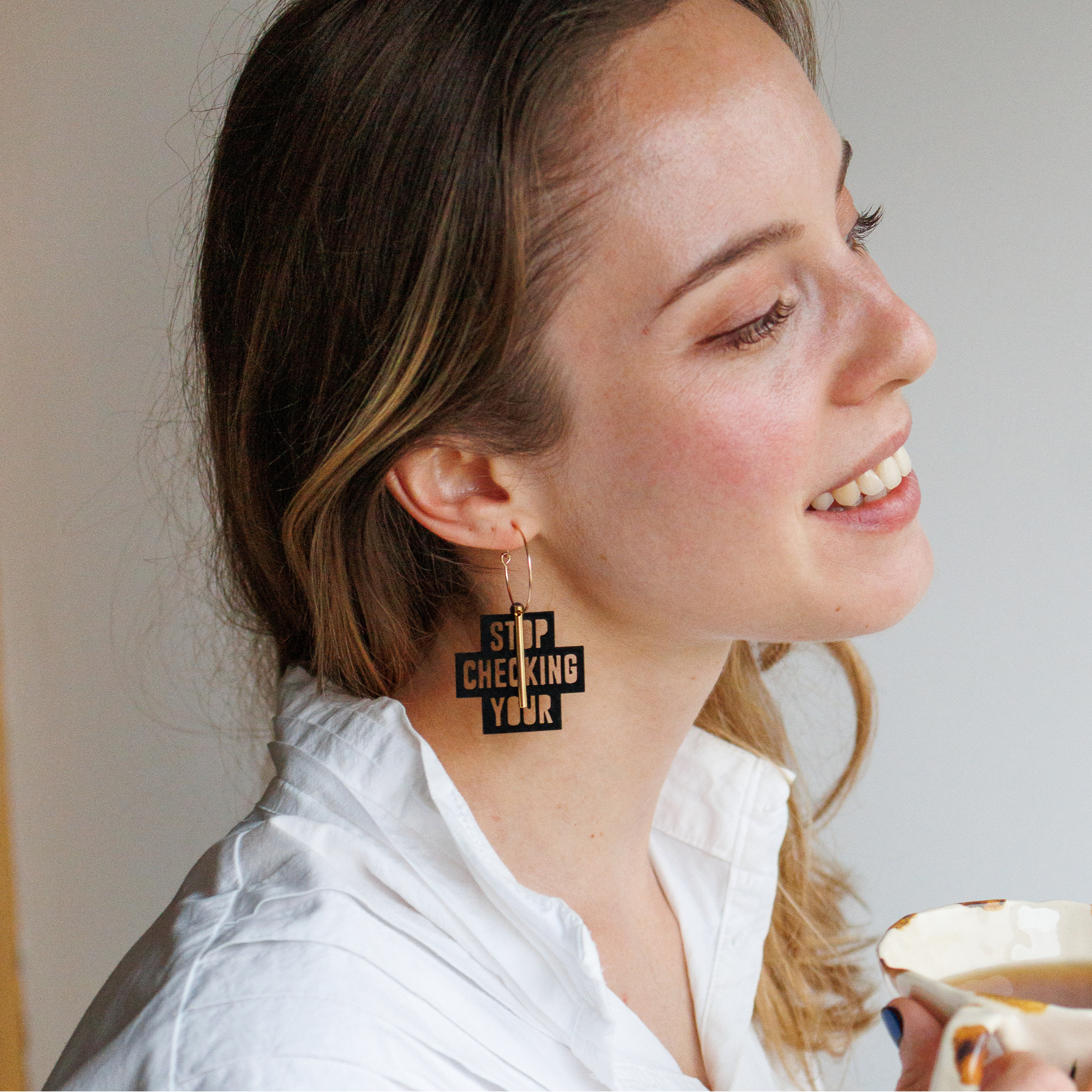 Femme souriante portant les creoles dorees Stop Checking Your Phone de Matcha Paris, bijoux ethique fabriques en France, style fun et engage.