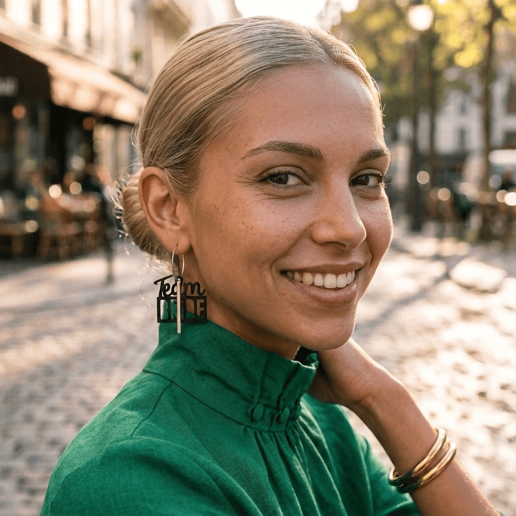 Boucles d'oreilles dépareillées Team Bride portées par une invitée EVJF, créole dorée charm texte, bijou mariage artisanal rock fait en France.
