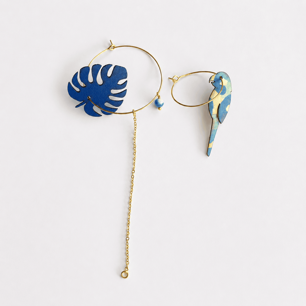 Packshot boucles d'oreilles dépareillées Massalia – créoles dorées monstera bleu cobalt et perroquet tropical liège – Matcha Bijoux