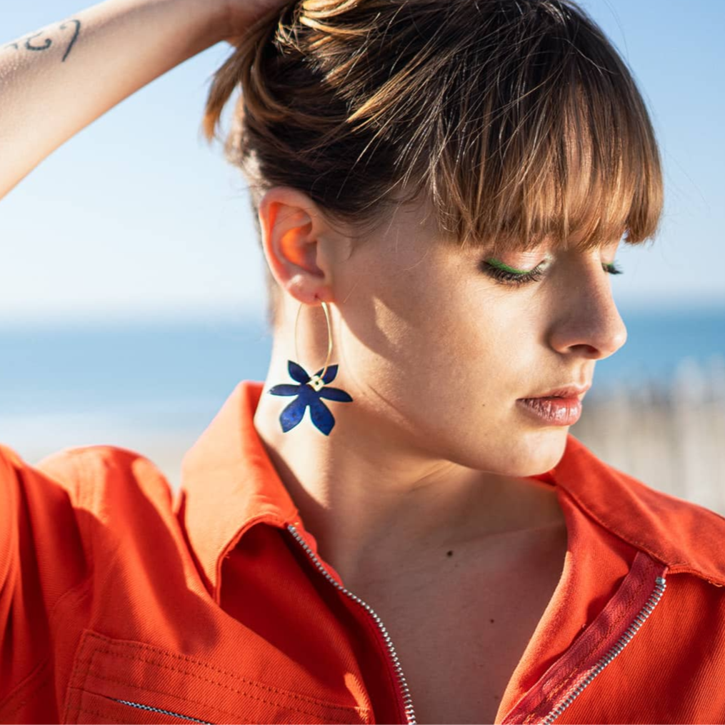 femme portant boucles d’oreilles dépareillées fleur bleu créoles asymétriques en acier inoxydable look été bord de mer style moderne