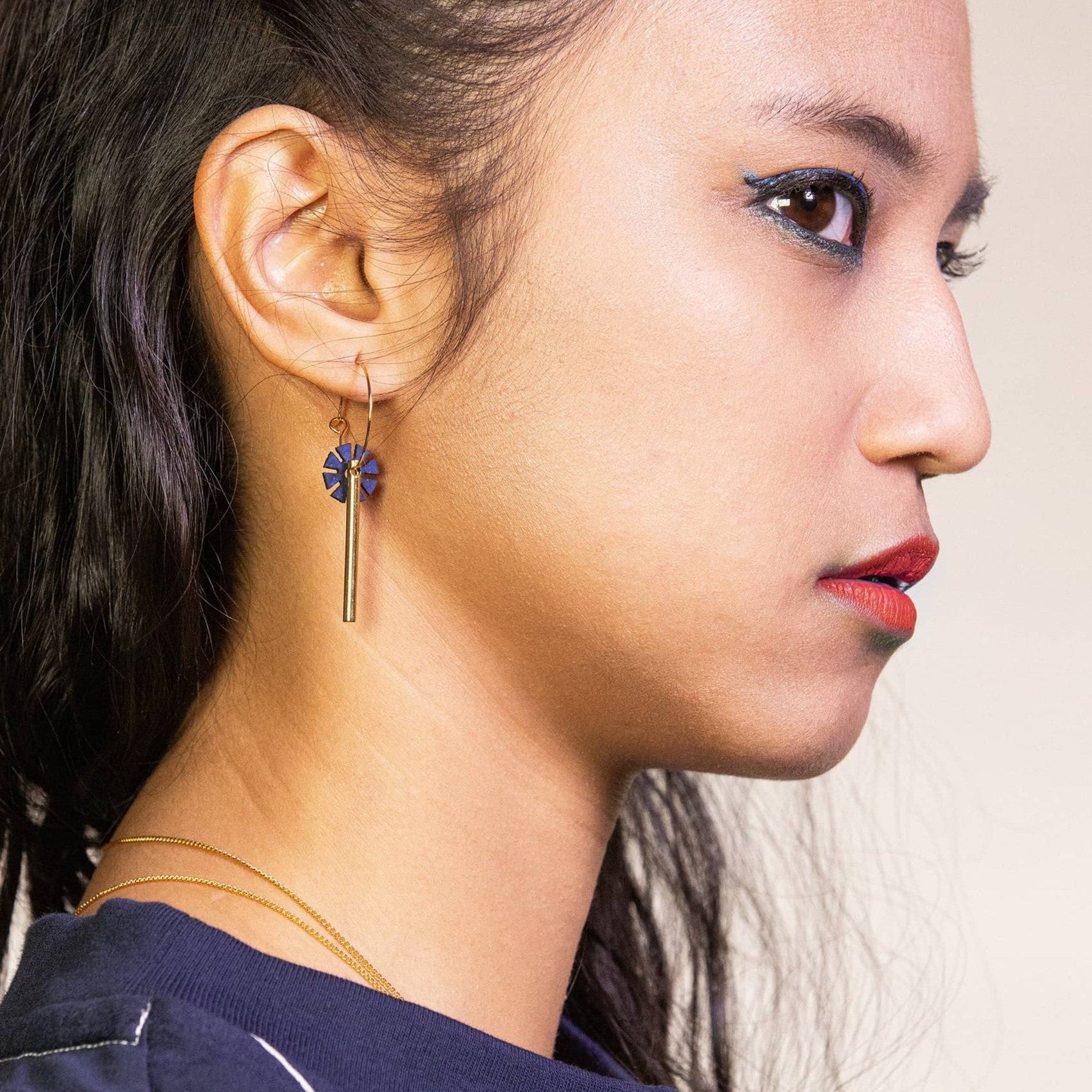 femme portant boucles d’oreilles dépareillées fleur bleu indigo avec tige dorée créoles asymétriques look moderne et élégant