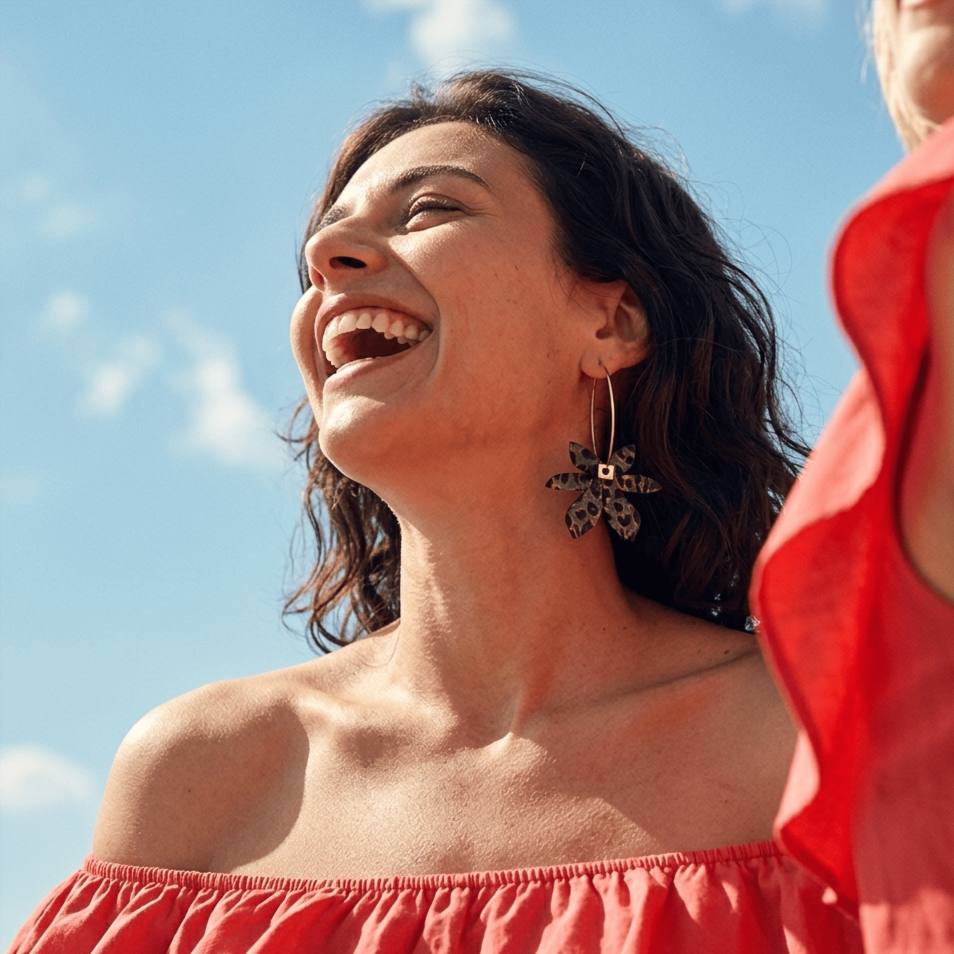 femme souriante portant boucles d’oreilles dépareillées léopard créoles asymétriques look été ciel bleu style mode