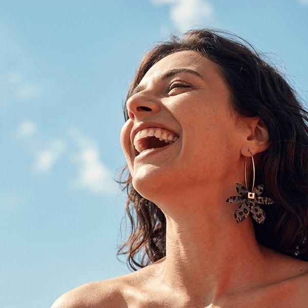 femme souriante portant boucles d’oreilles dépareillées léopard créoles asymétriques look été ciel bleu style mode