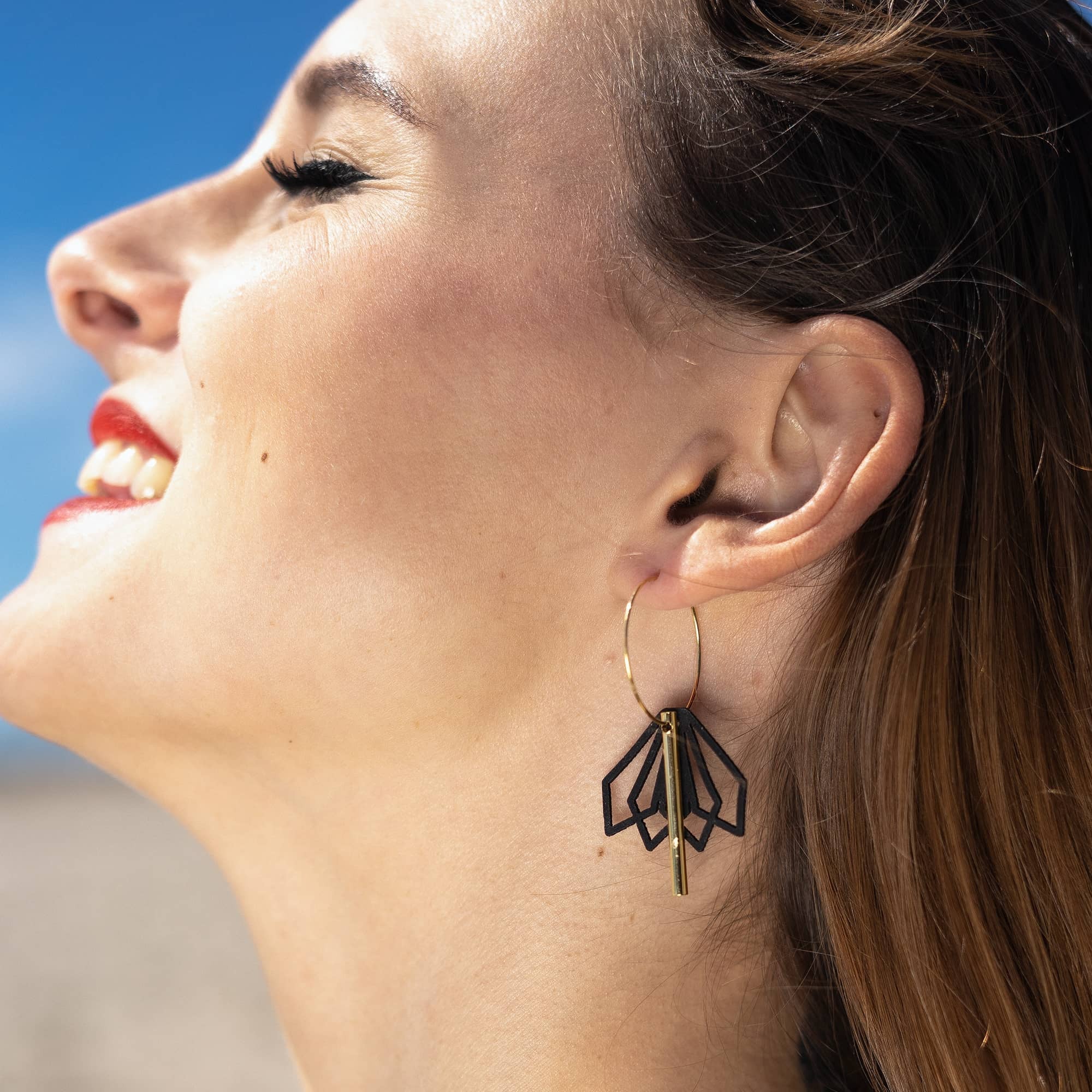 femme portant boucles d’oreilles dépareillées noires créoles asymétriques en acier inoxydable design graphique look été lumineux style moderne