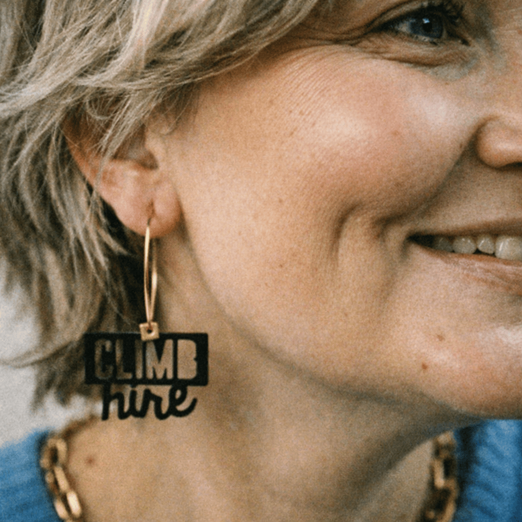 Boucle d’oreille Capricorne portée par une femme, créole dépareillée avec message « Climb higher ».