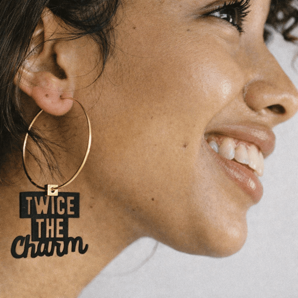 Boucle d’oreille Gémeaux portée par une femme, créole dépareillée avec message « Twice the charm ».