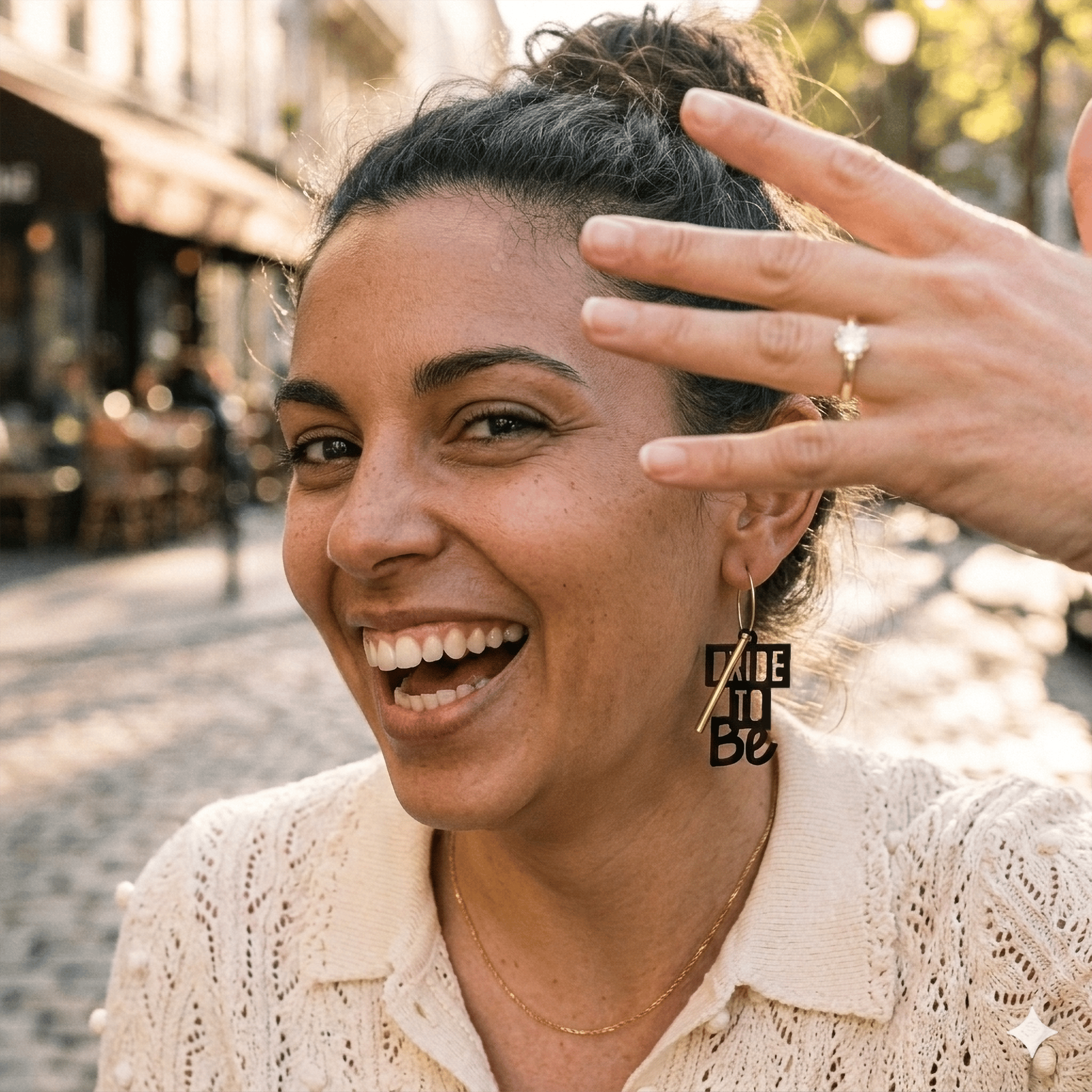 Boucles d'oreilles dépareillées Bride to Be portées par une mariée souriante, créole dorée charm texte, bijou EVJF artisanal rock fait en France.