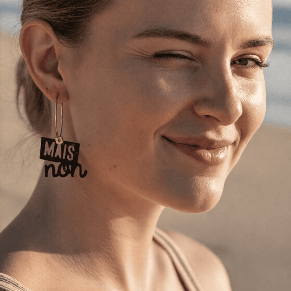 Femme portant des boucles d oreilles depareillees Mais non, creoles asymetriques en laiton dore avec message graphique noir, bijou original et tendance.