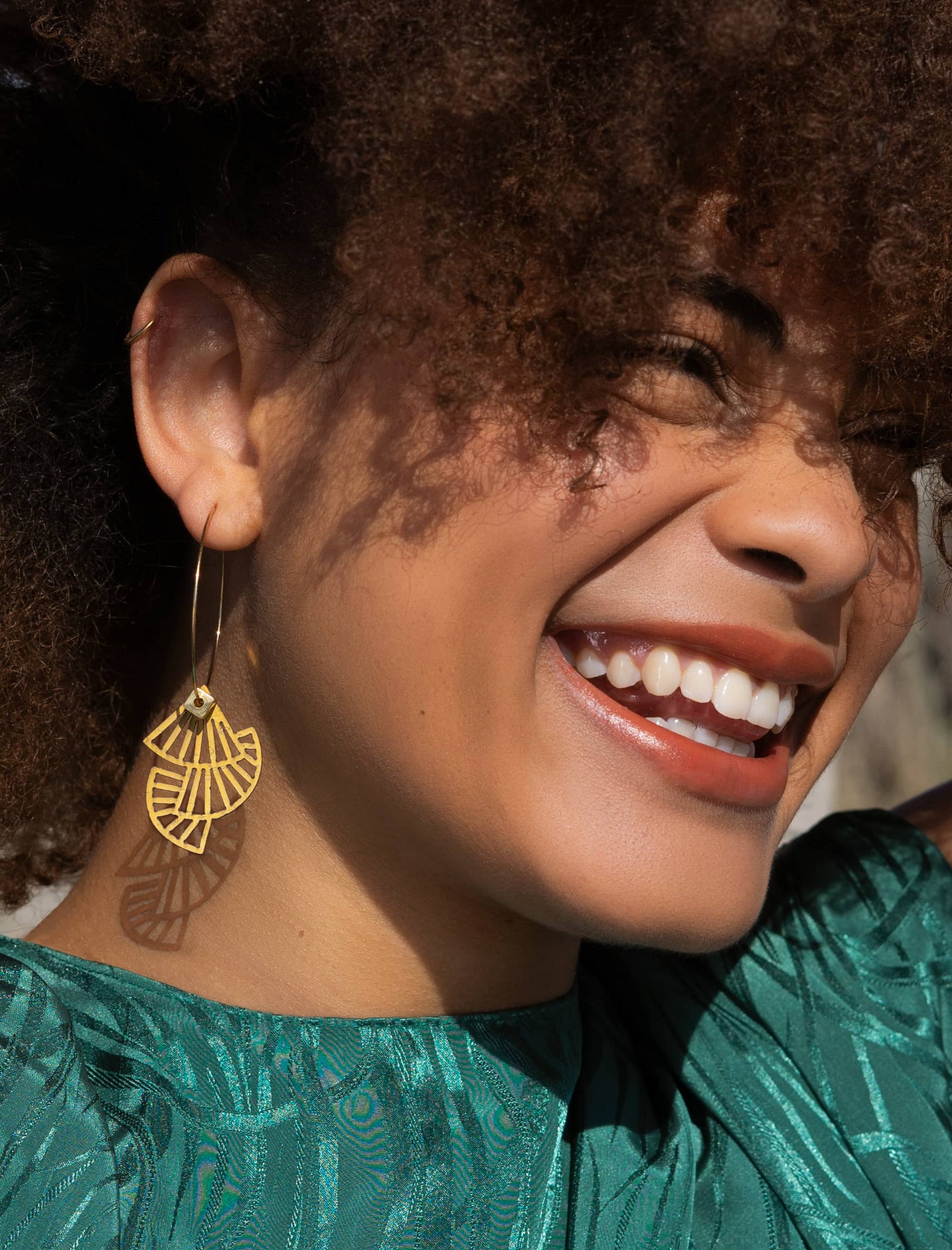 Femme souriante portant une créole dorée géométrique Matcha Paris – bijou personnalisable et fabriqué en France, en matières écoresponsables.