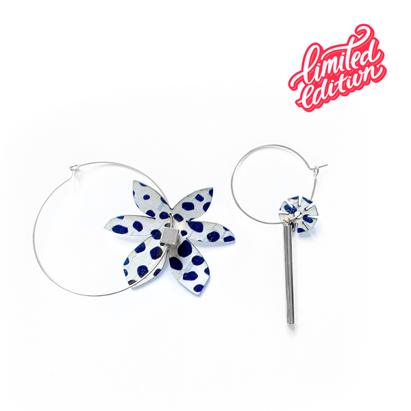 Paire de créoles dépareillées Matcha Paris en édition limitée, avec breloques à motifs pois bleu sur fond blanc, en forme de fleur et barre verticale argentée.