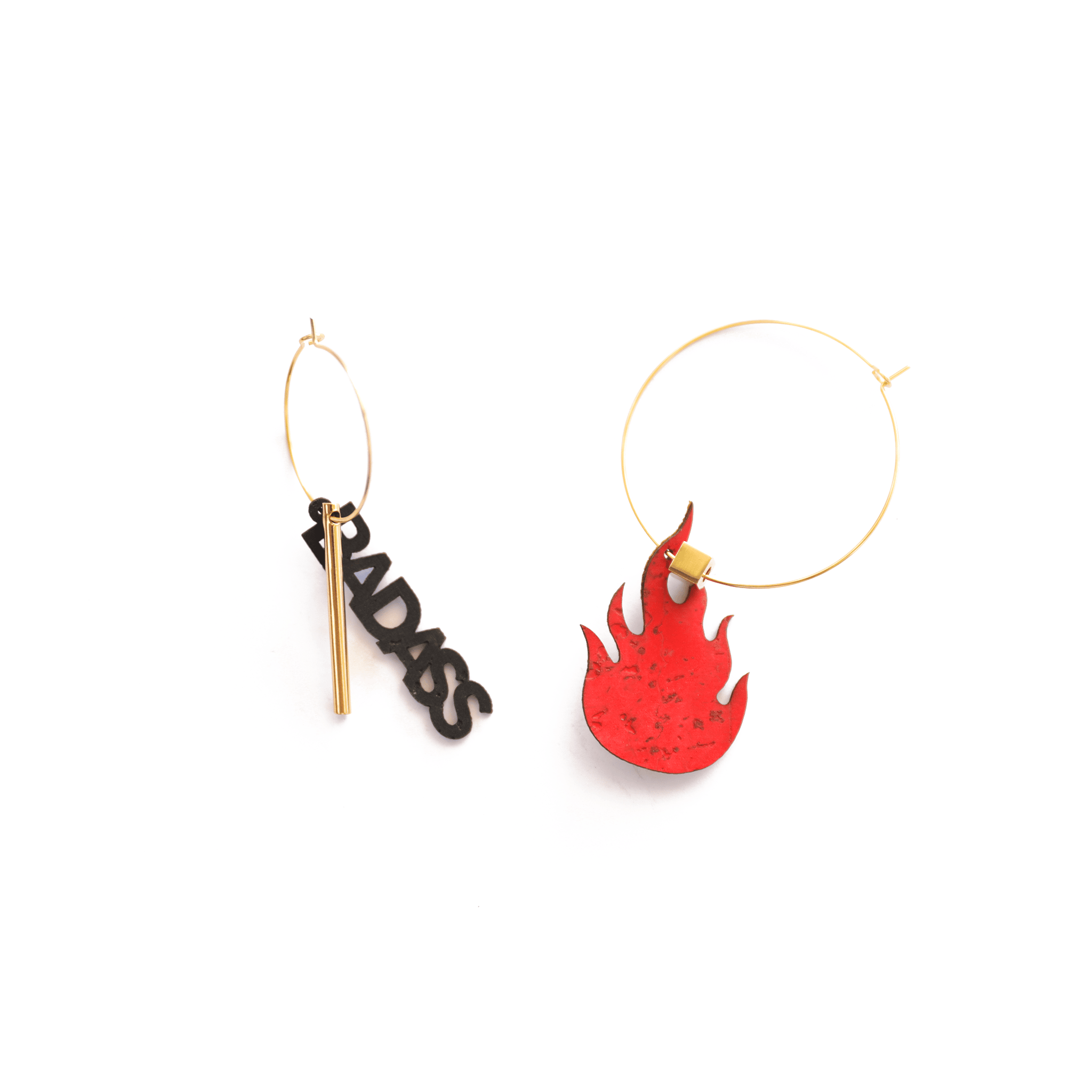 Paire de créoles dorées asymétriques : l’une ornée du mot "BADASS" en lettres noires avec une barre dorée, l’autre d’une flamme rouge en liège. Bijoux audacieux fabriqués en France, en matériaux vegan et éthiques.